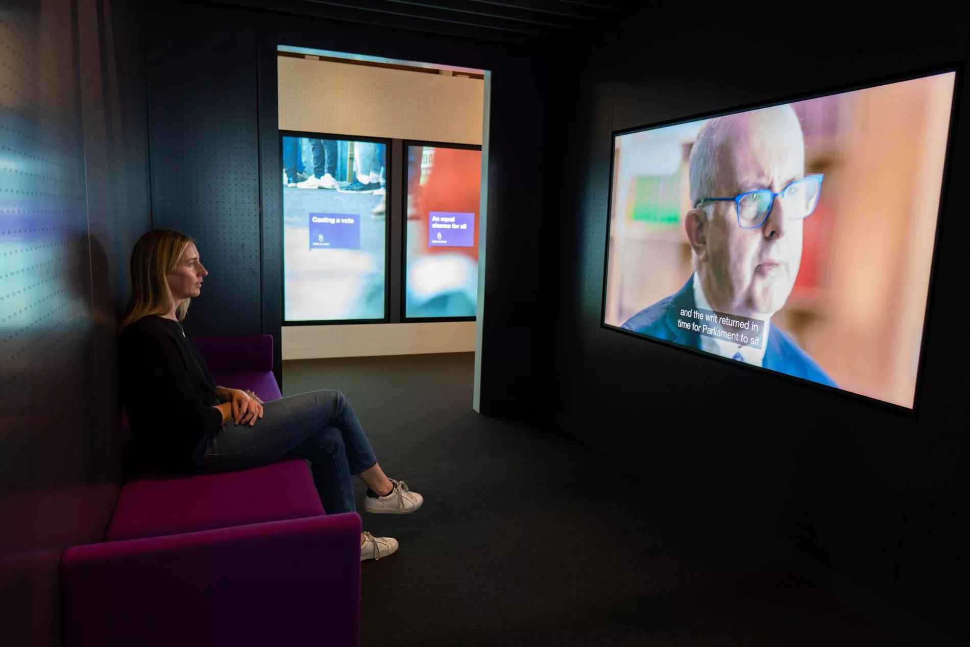 A woman is sitting and viewing a large screen in an exhibition.