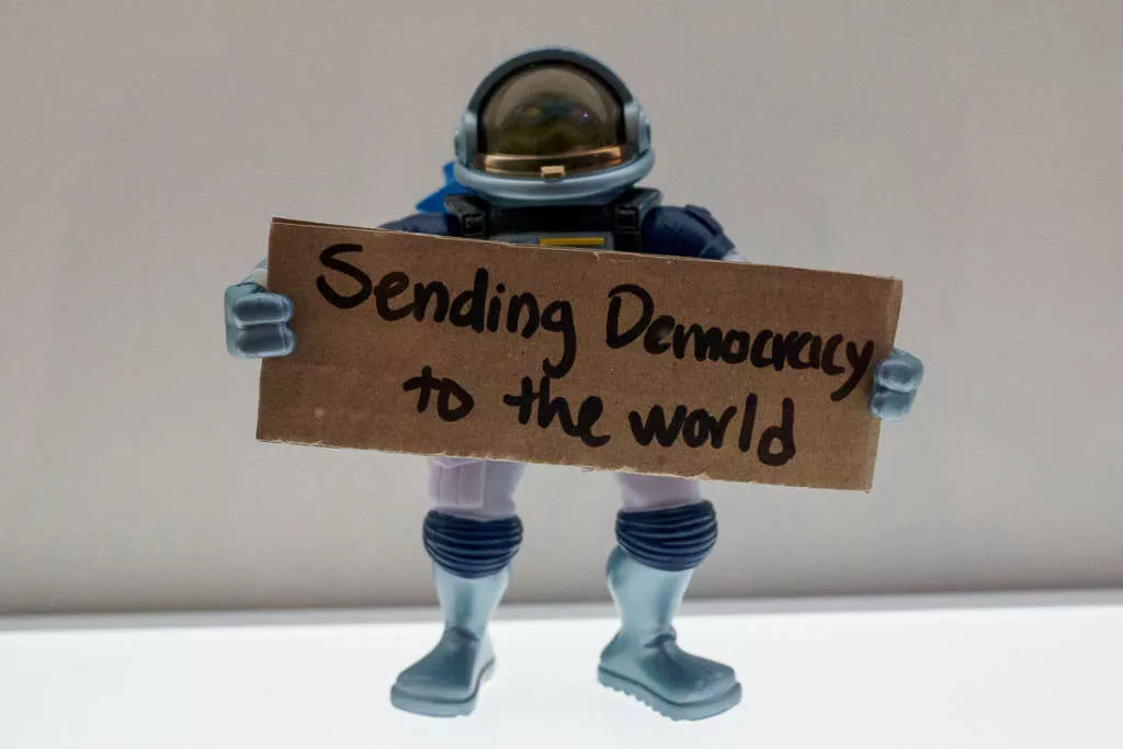 A toy holds a sign that says 'Sending democracy to the world. A toy holds a sign that says 'Sending democracy to the world.