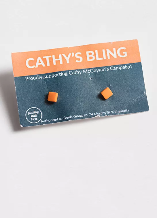 Photograph of two small, square orange earrings.