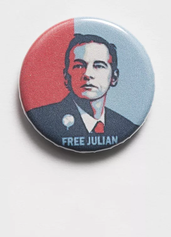 Photograph of a badge with an illustration of Julian Assange and the label "Free Assange"