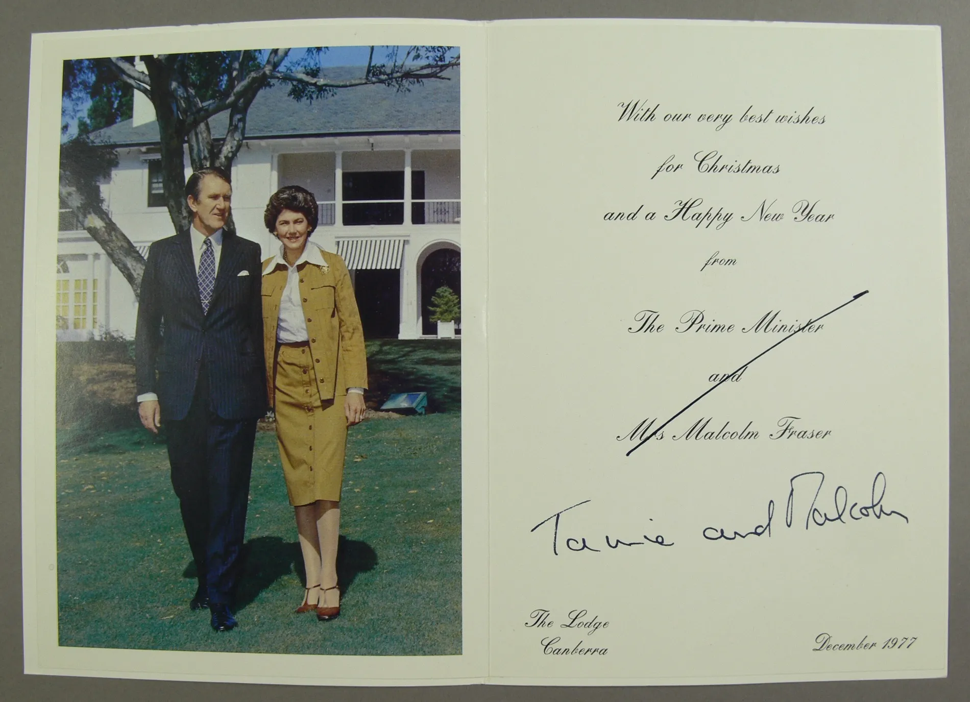 A Christmas card featuring a photo of Malcolm Fraser wearing a dark blue pinstripe suit and Tamie Fraser wearing a tan safari suit and white blouse, posing in front of their home. 