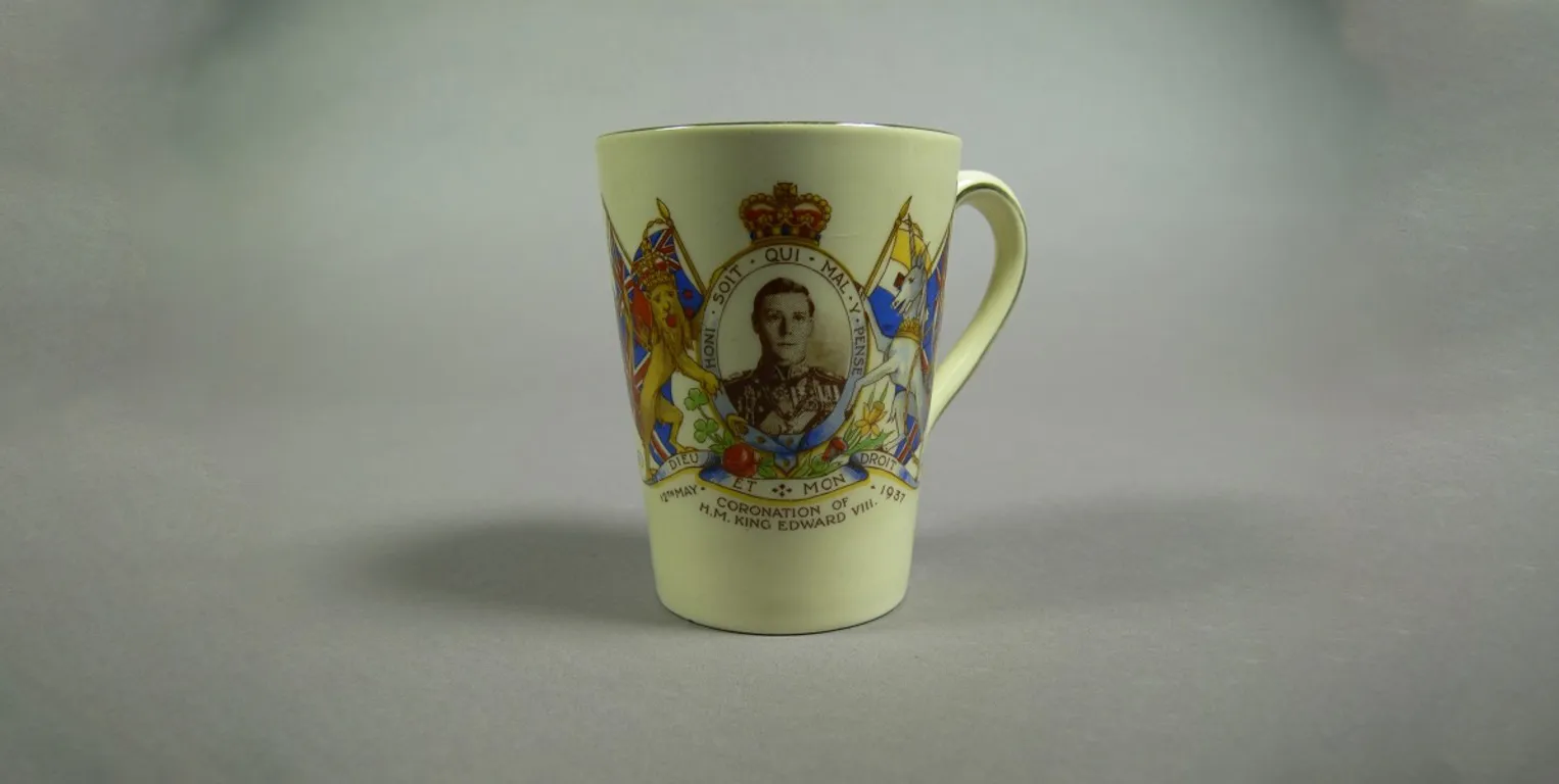 A ceramic mug featuring a portrait of Prince Edward, framed with the British coat of arms, with the words 'Coronation of H.M. King Edward VIII' and '12th May 1937'. A ceramic mug featuring a portrait of Prince Edward, framed with the British coat of arms, with the words 'Coronation of H.M. King Edward VIII' and '12th May 1937'.