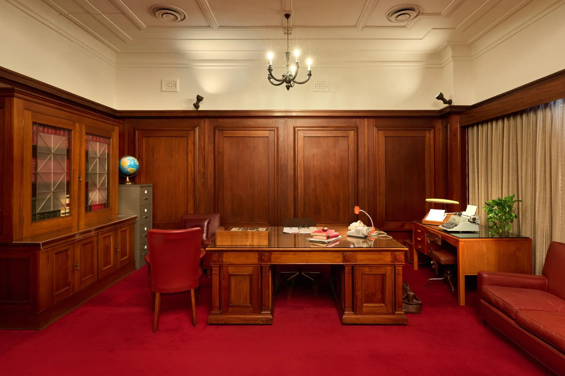 An office at Old Parliament House with red carpet, a large wooden desk, red leather chairs, wood panelled-walls and a book case.