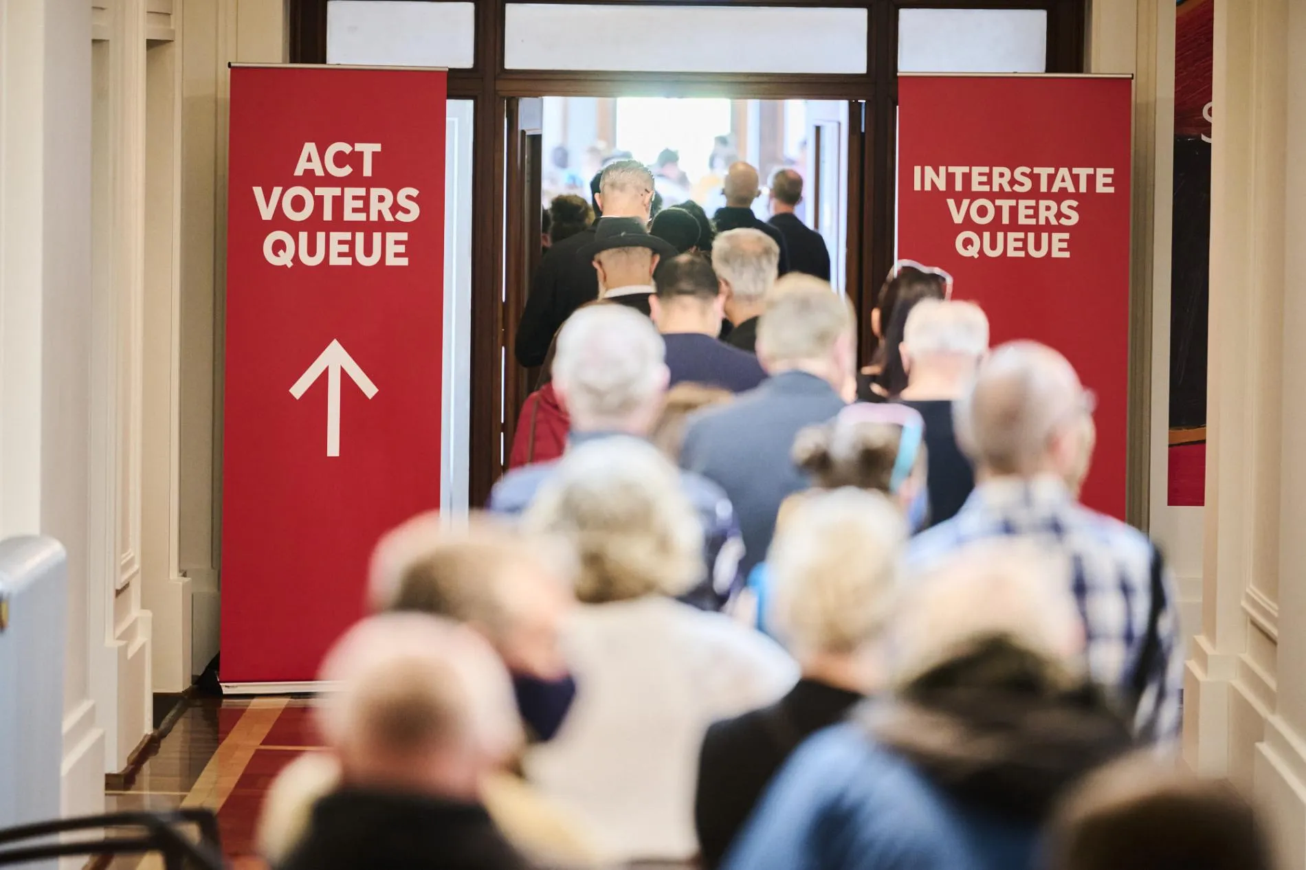 Two red banners, one directing ACT voters and one for interstate voters stand on either side of a doorway filled with people in Old Parliament House.