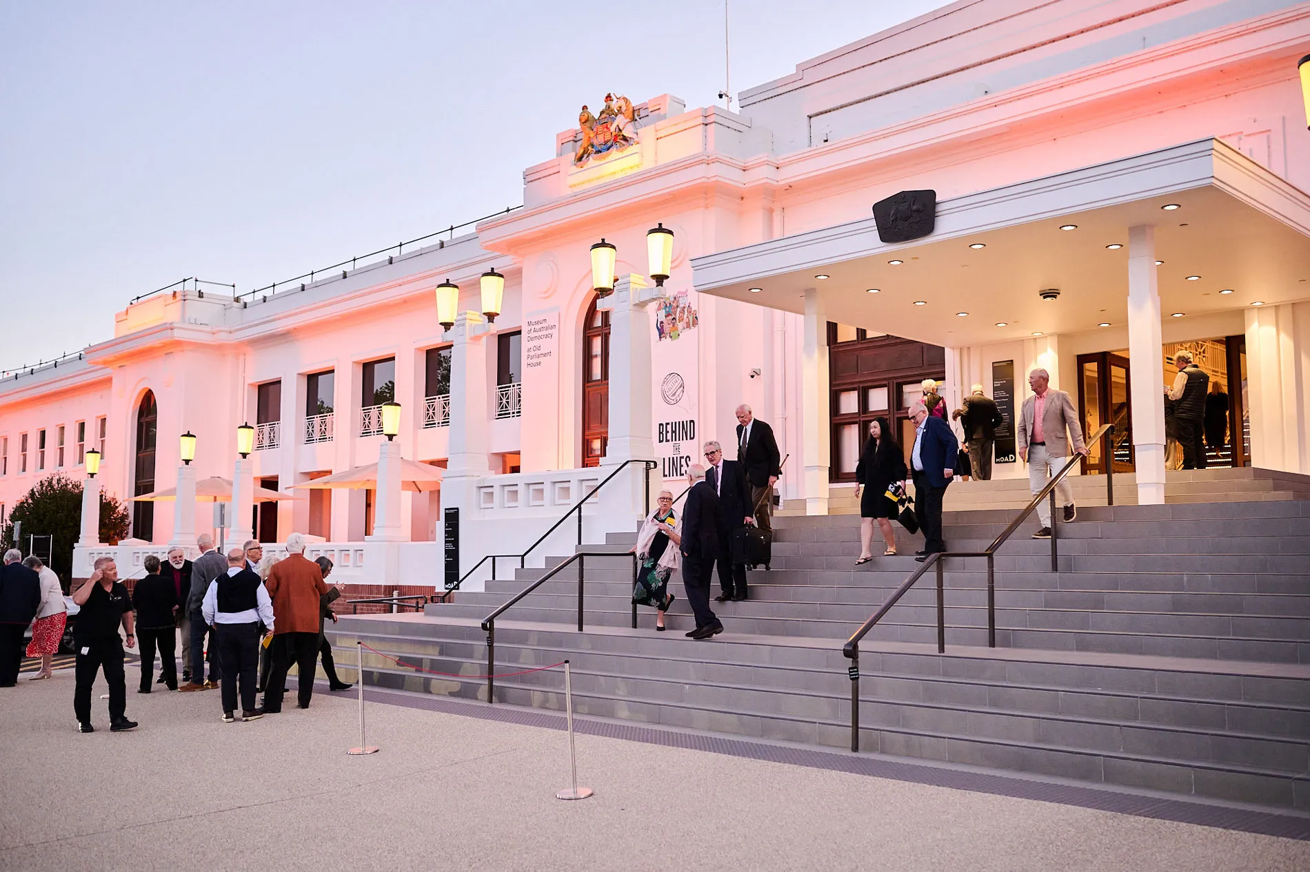 People descending the steps of Old Parliament House at twilight.