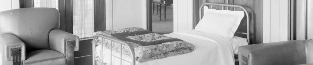 A black and white photo of a single bed in a room