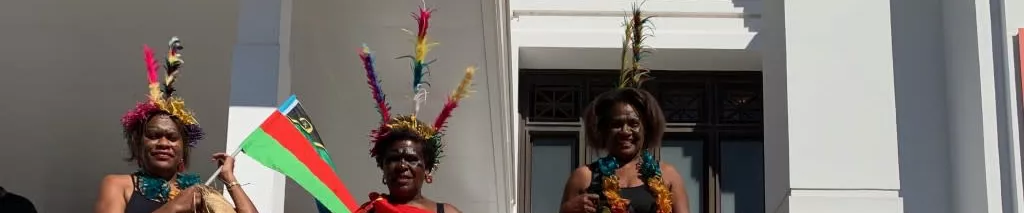 (Waskam) Emeled Davis stands on the front steps of Old Parliament House holding a flag.