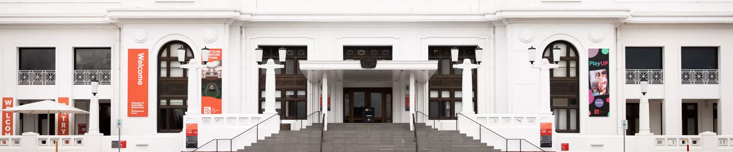 A large staircase leads up to a white old building with a flag on the top.