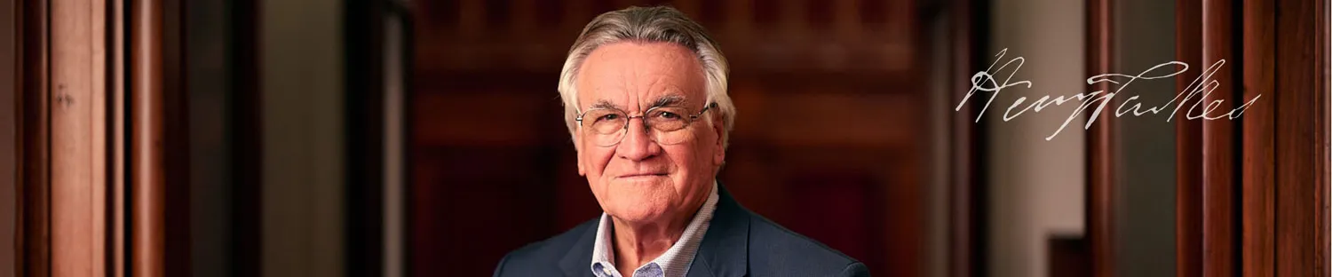 Barrie Cassidy wears a blue suit with light blue shirt. He is standing in Old Parliament House in an ornate wooden doorway.