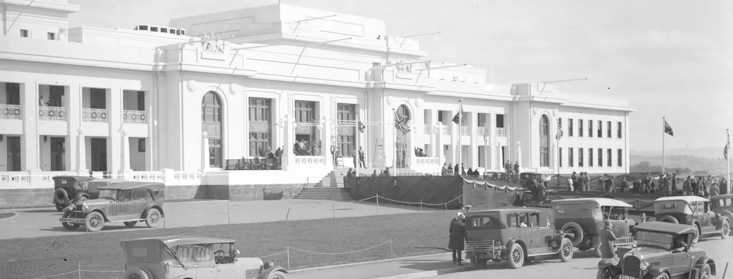 A black and white photo from 1927 of a large white building, Old Parliament House, with cars driving past.