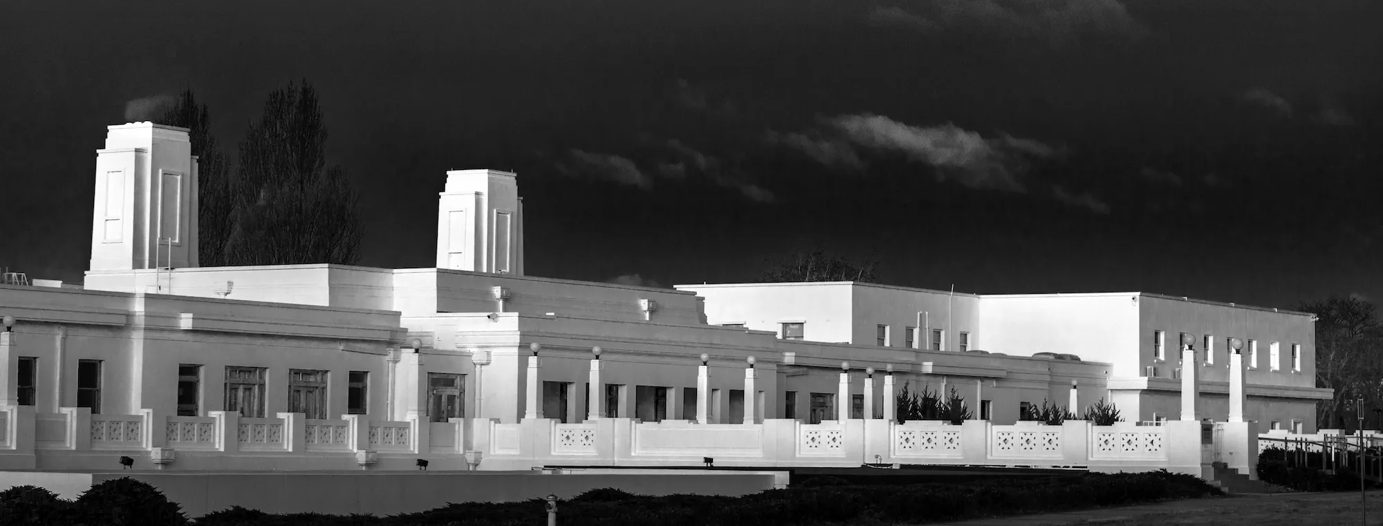 A long white building, Old Parliament House, with a dark sky and the moon in the background.