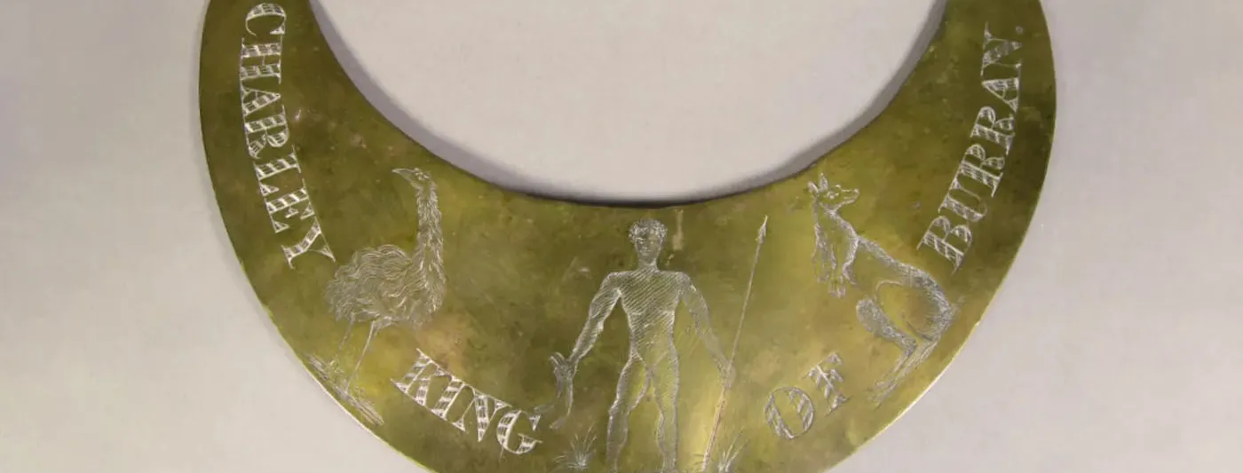 A brass breastplate with the words 'CHARLEY KING OF BURRAN' etched with illustrations of an emu, kangaroo, and a man holding a spear and two burren (boomerangs).