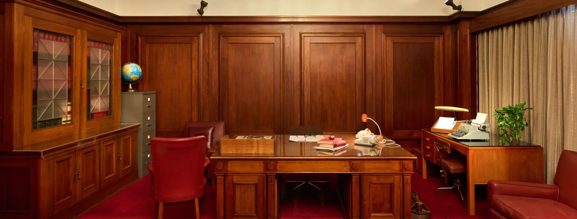 An office at Old Parliament House with red carpet, a large wooden desk, red leather chairs, wood panelled-walls and a book case.