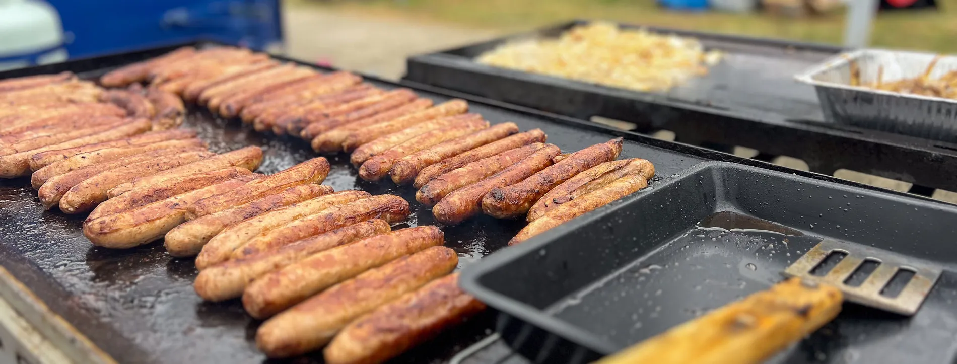 Sausages are lined up in two rows on a barbecue plate at an outdoor fundraising sausage sizzle at Old Parliament House.