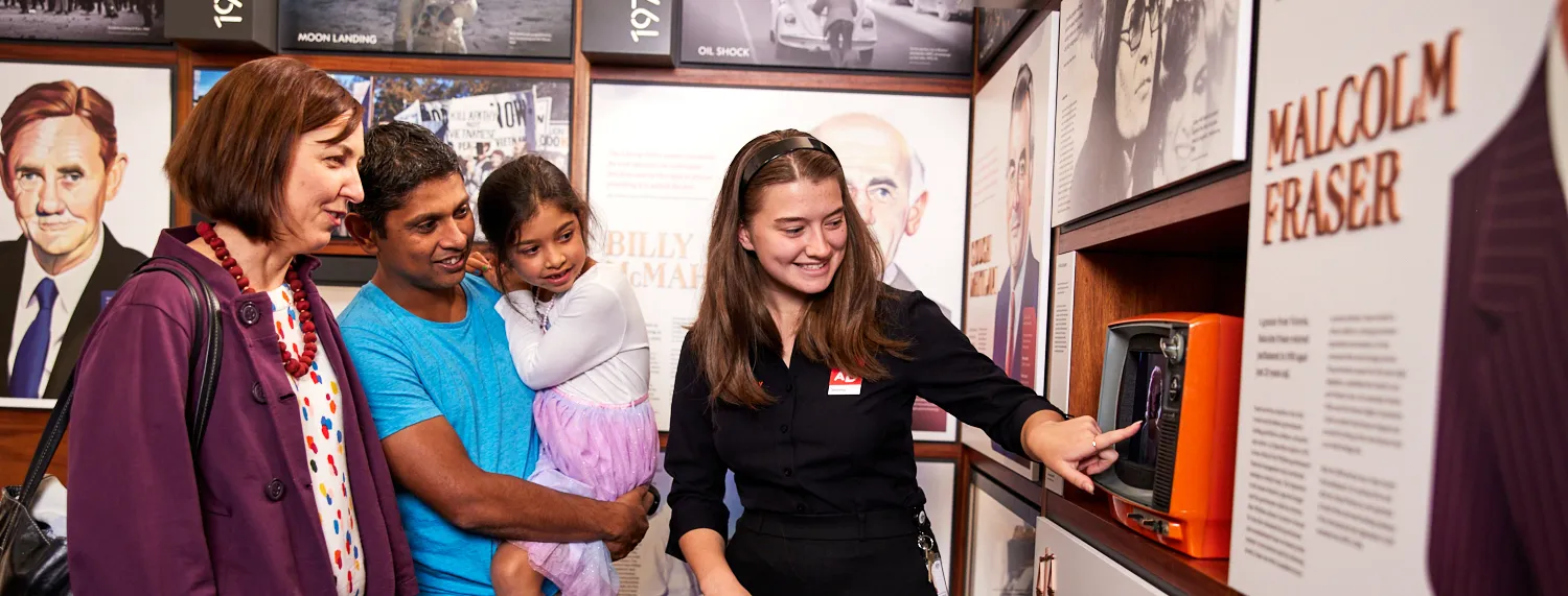 A family and a museum staff member look at an old-fashioned orange television set in an exhibition featuring Australian prime ministers at Old Parliament House.