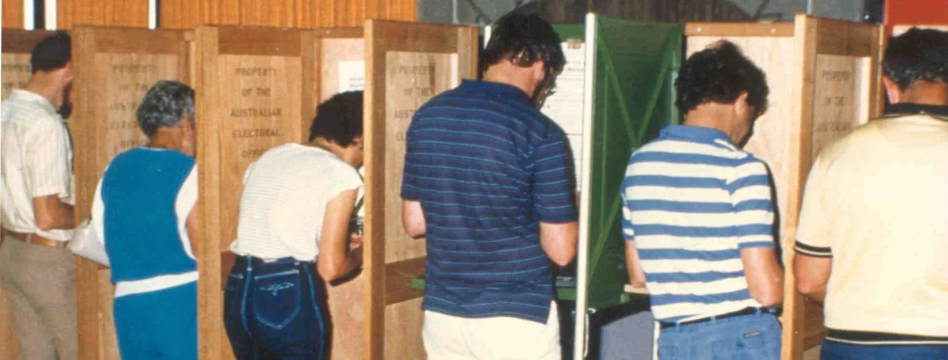 Men and women dressed in 1970s fashion vote in partitioned booths which are labelled 'Property of the Australian Electoral Office'.