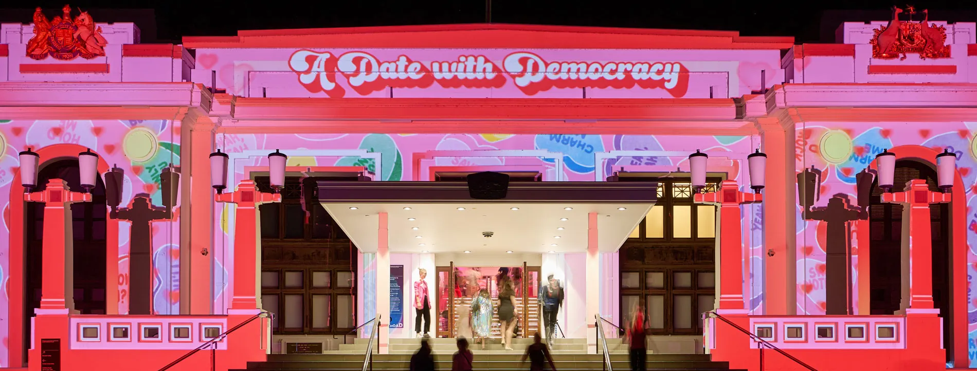 Pink and red illuminates the front of Old Parliament House. Text in white and red above the entrance reads 'A date with democracy'.