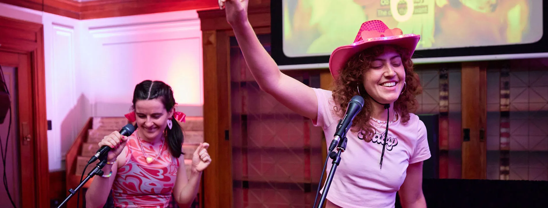 Two women wearing pink dance in front of microphones in Old Parliament House.