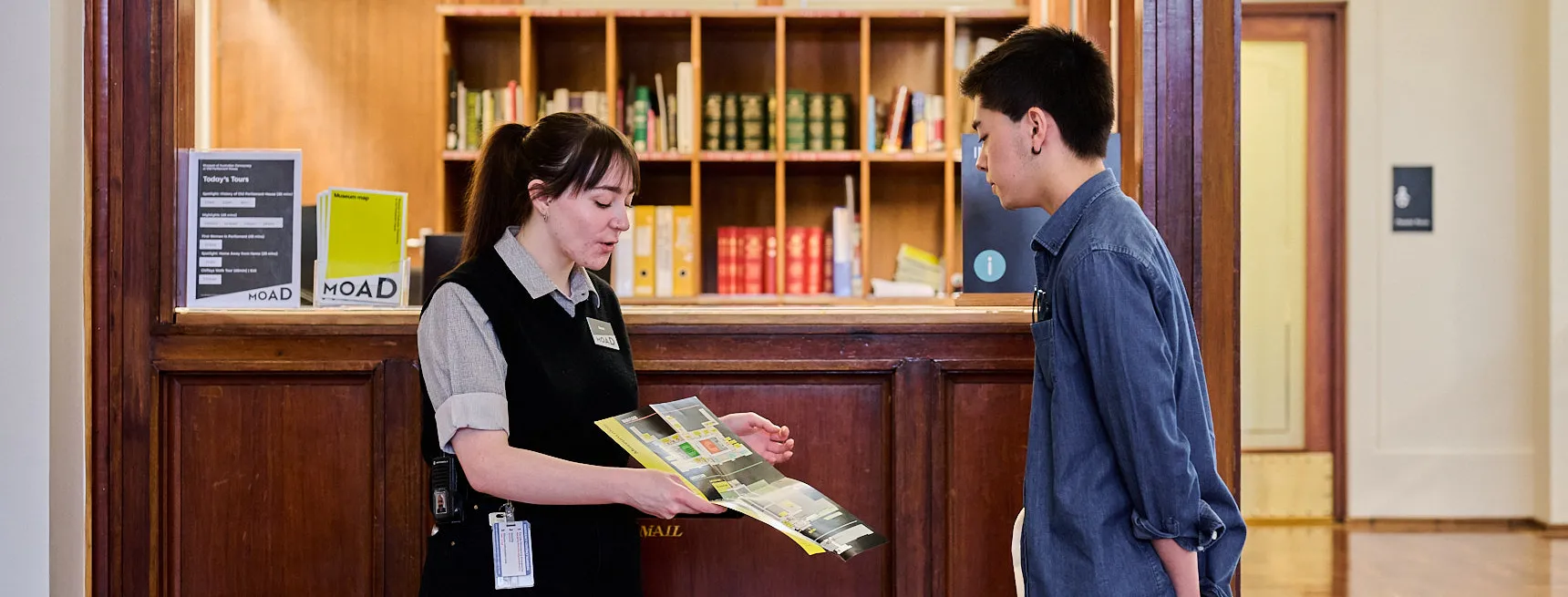 An Old Parliament House museum staff member stands in King's Hall showing a visitor a map.