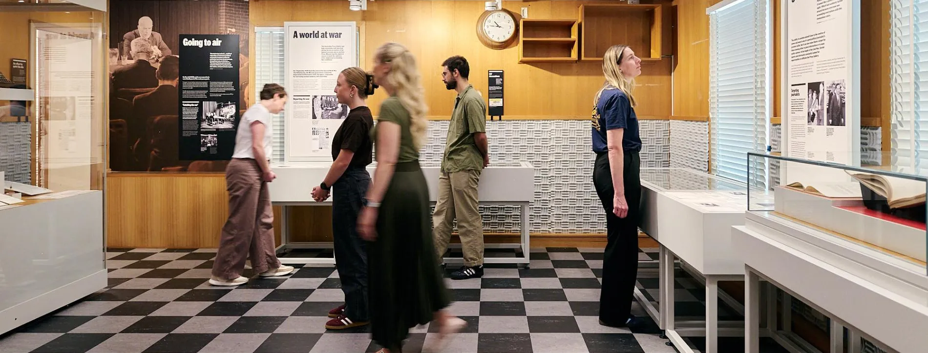People stand on black and white tiled floor in the Press Gallery exhibition in Old Parliament House.