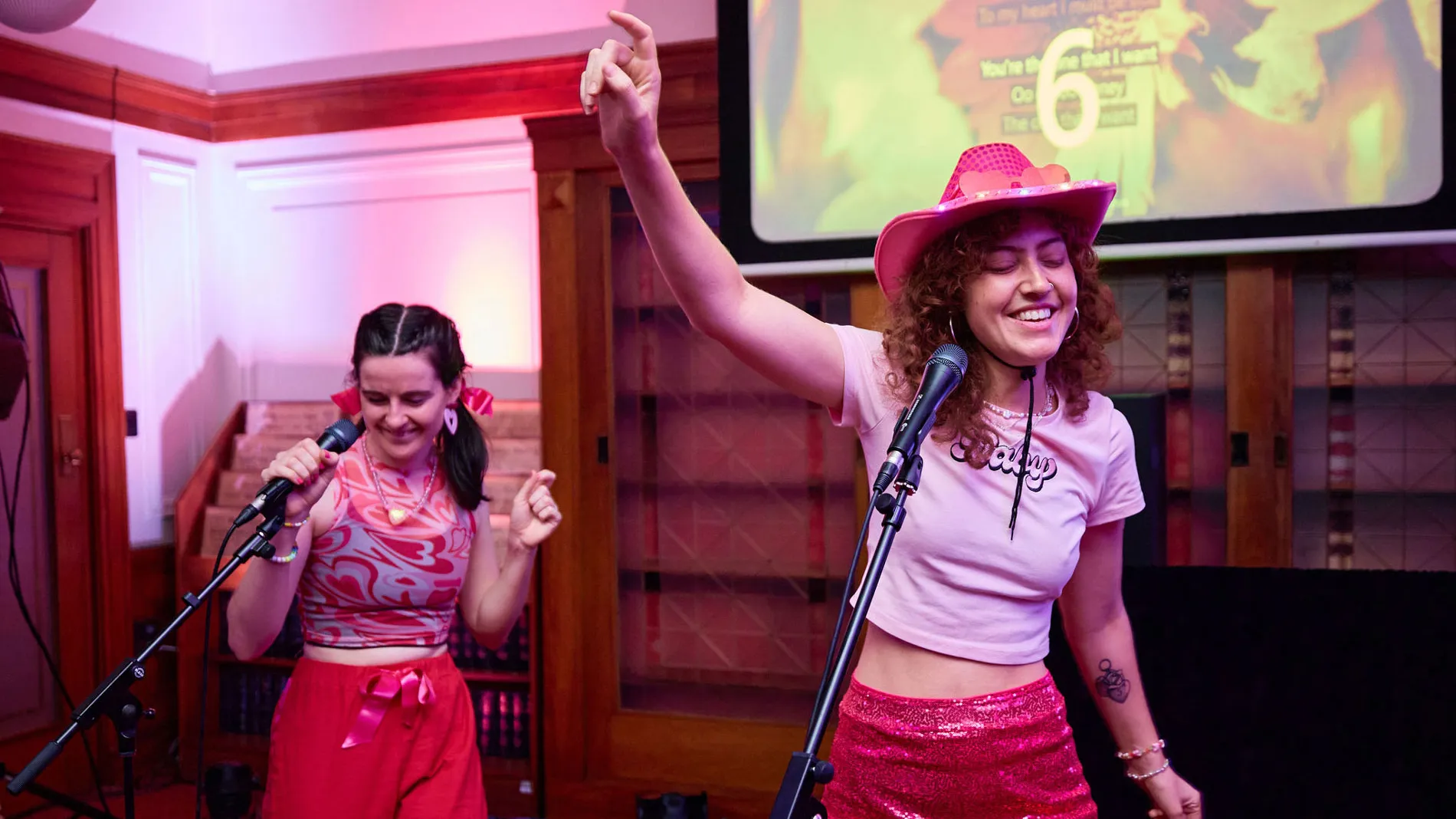 Two women wearing pink dance in front of microphones in Old Parliament House.