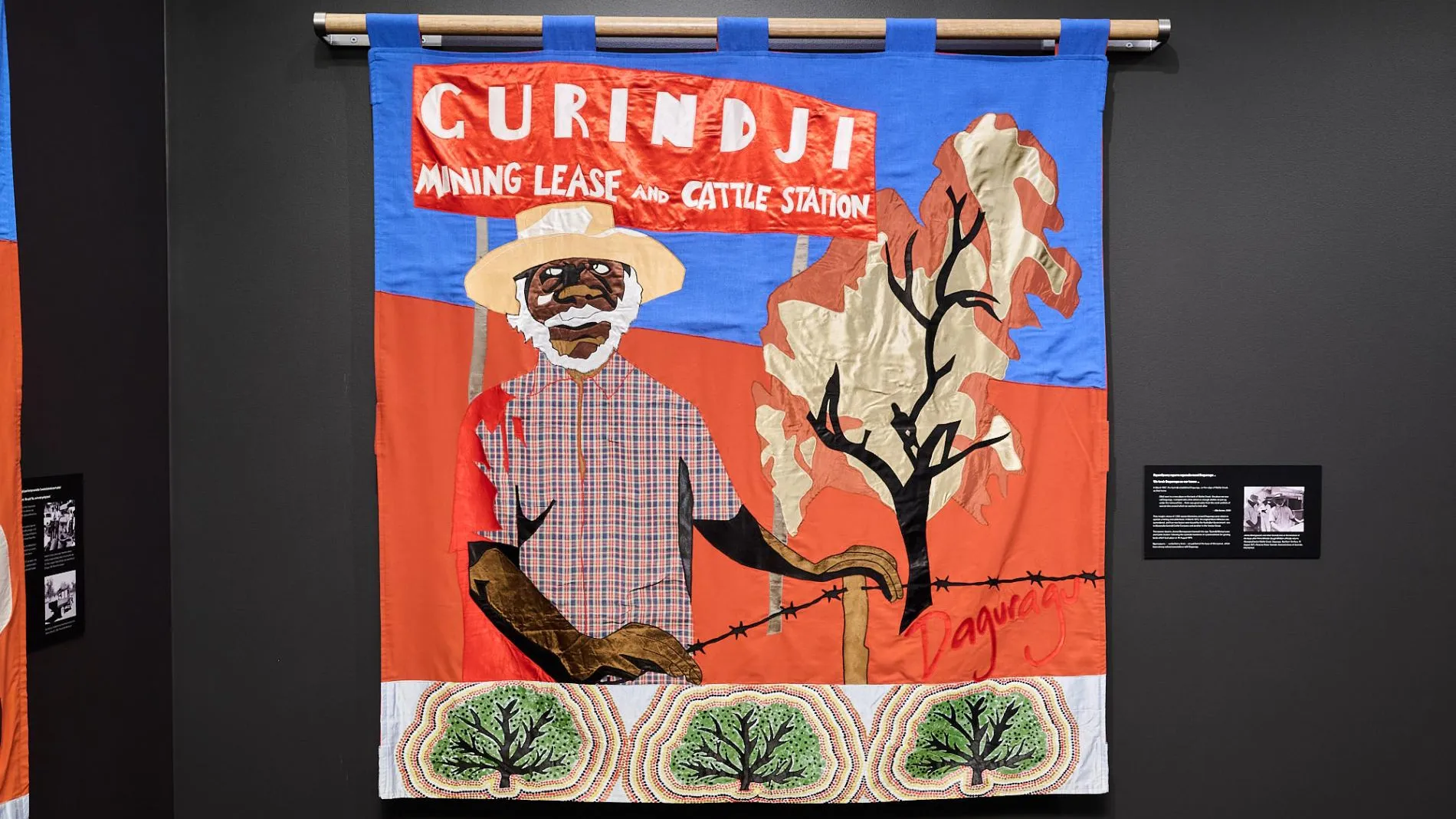 A Gurindji freedom banner depicting a First Nations person. The banner hangs in the exhibition on a black wall in Old Parliament House.