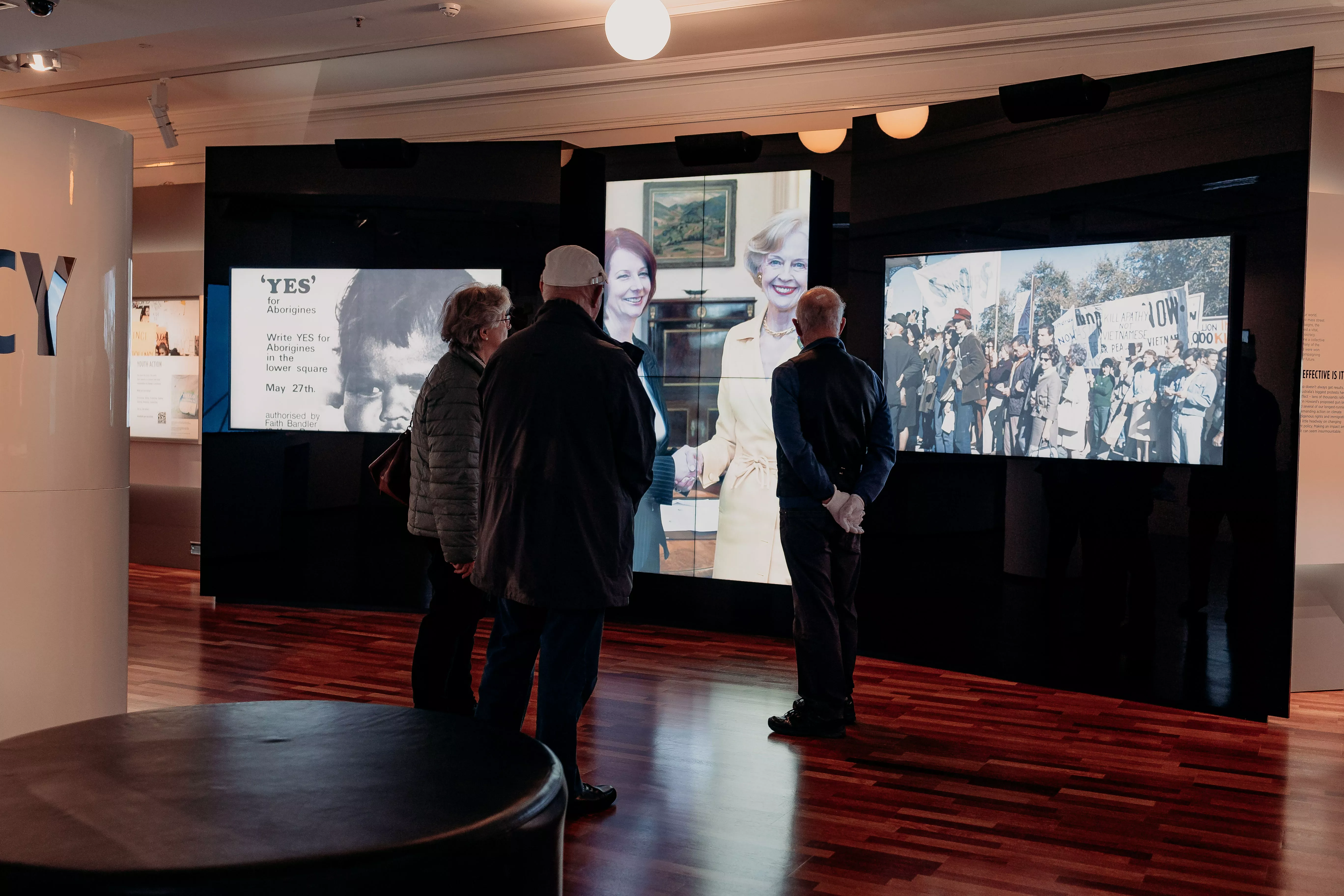 The silhouettes of three people from behind as they stand in front of 3 large video screens in an exhibition. The silhouettes of three people from behind as they stand in front of 3 large video screens in an exhibition.