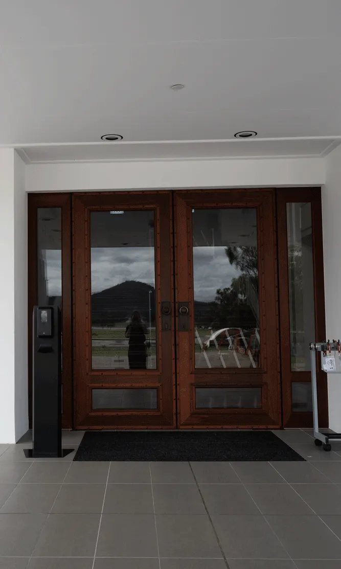 An entrance to a building with large glass double doors with wooden frames. An umbrella stand sits to the right. A black sign says 'Welcome to MoAD'.