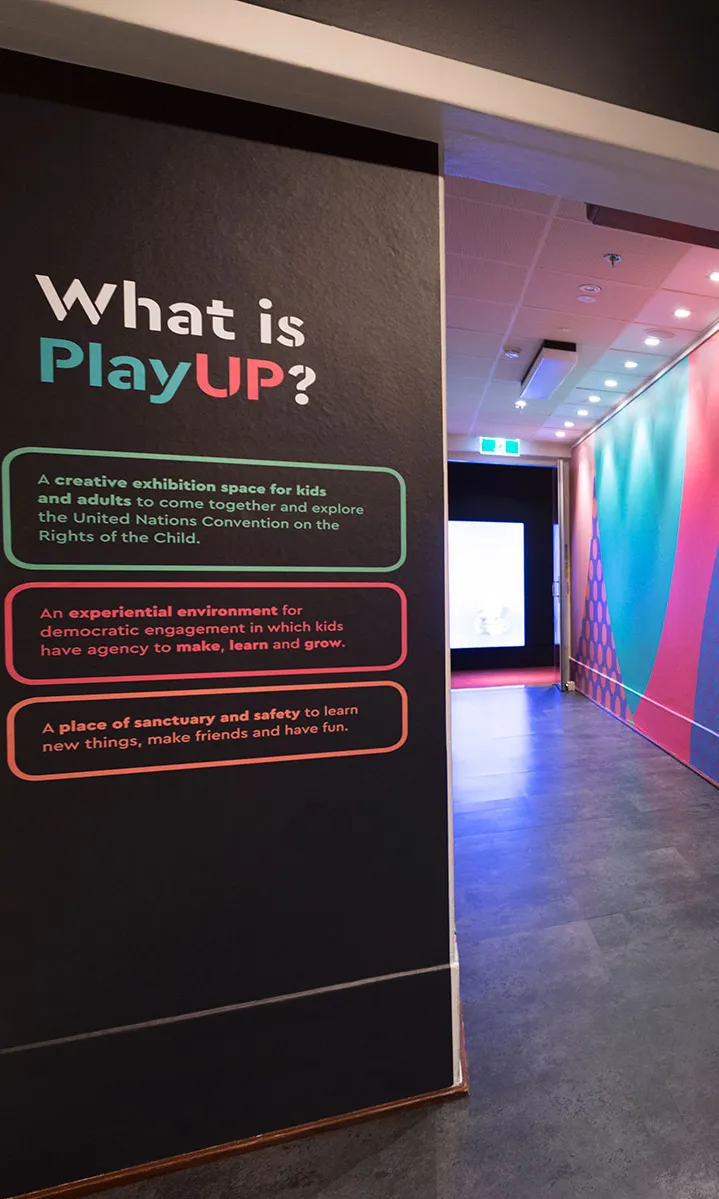 The entrance to PlayUP at MoAD where there are black walls with brightly coloured text and images.