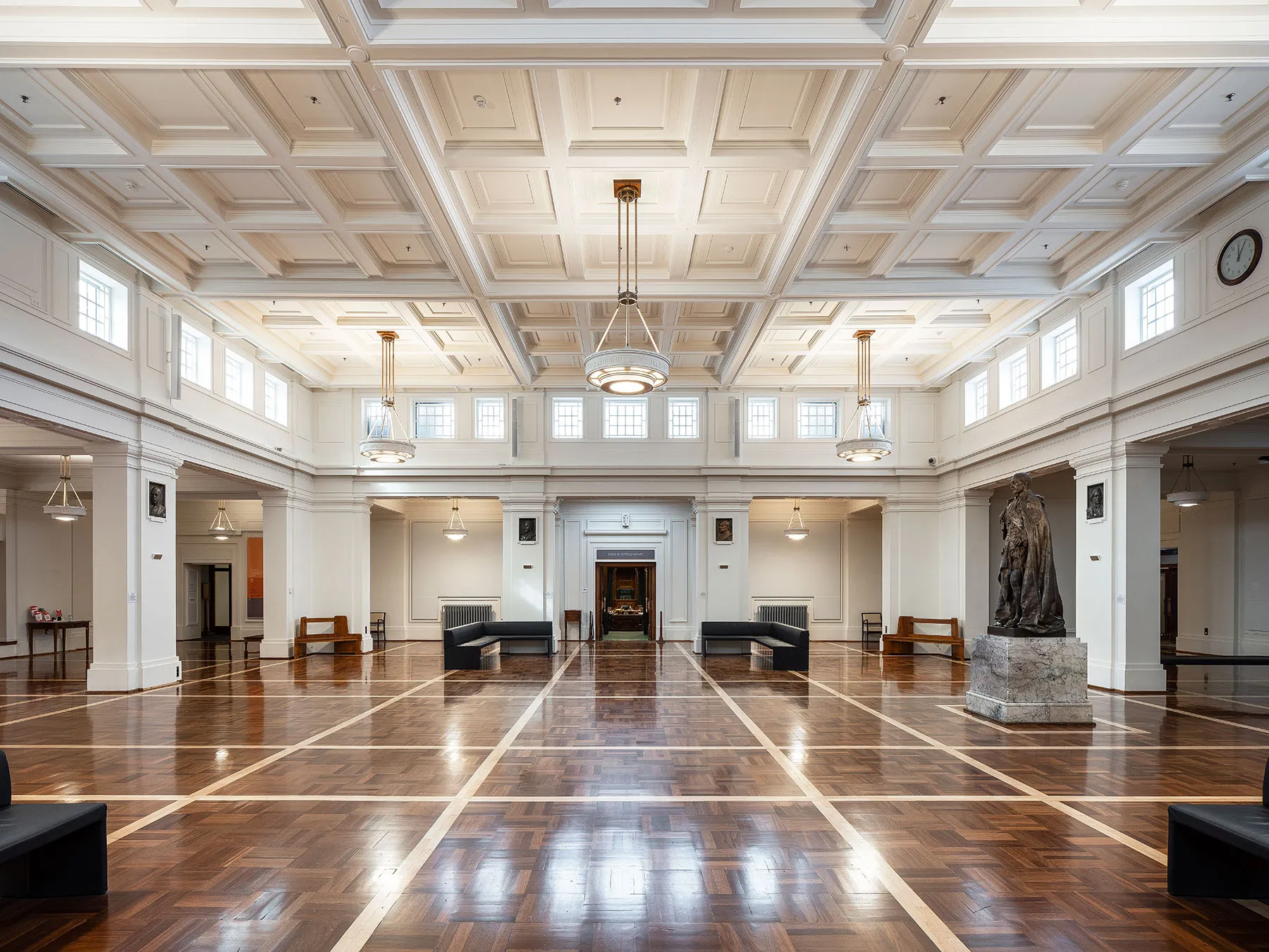 King's Hall at MoAD at Old Parliament House featuring parquetry floors, a statue, couches and hanging lights from an ornate ceiling.