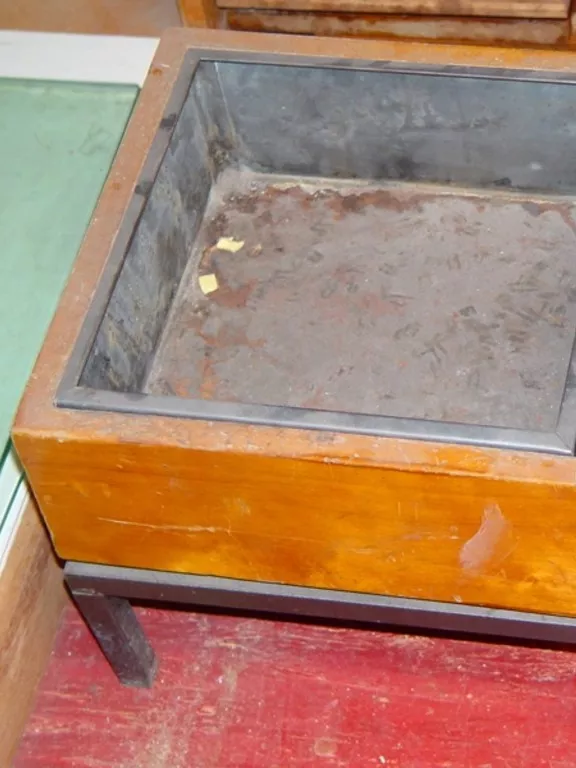 A square wooden ashtray with a metal insert and sitting on a metal base with four small legs.