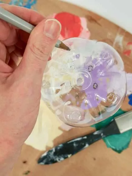 A close up of a hand holding a paintbrush over a water bottle on top of a paint palette.