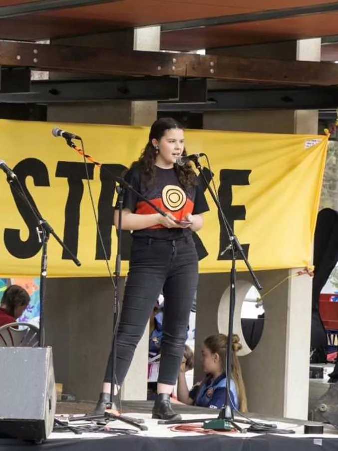 Dhani Gilbert speaks into a microphone, on stage, for a school strike for climate change protest