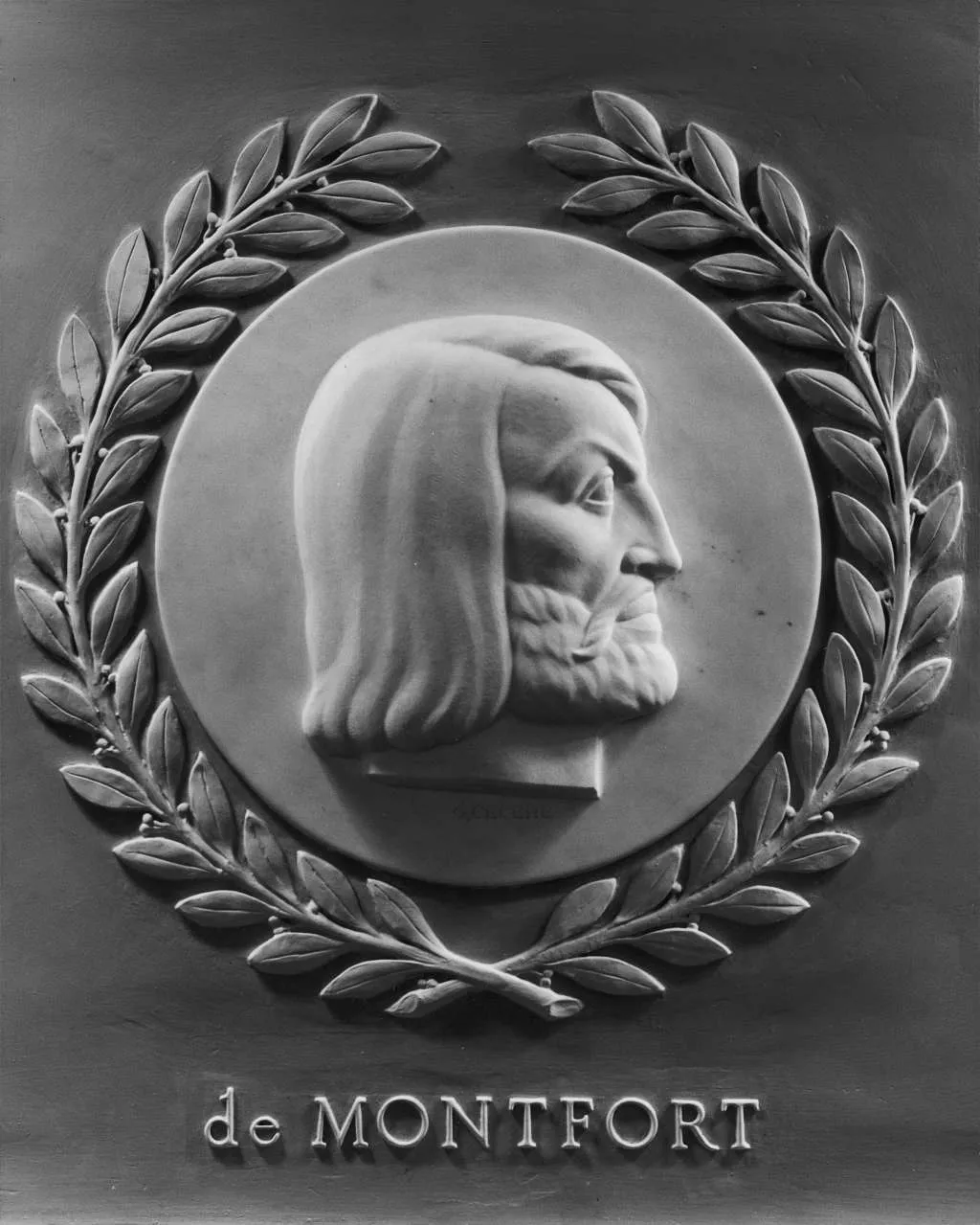 A carved profile of a man's head with long hair and beard, framed with a laurel wreath with the words 'de MONTFORT'.