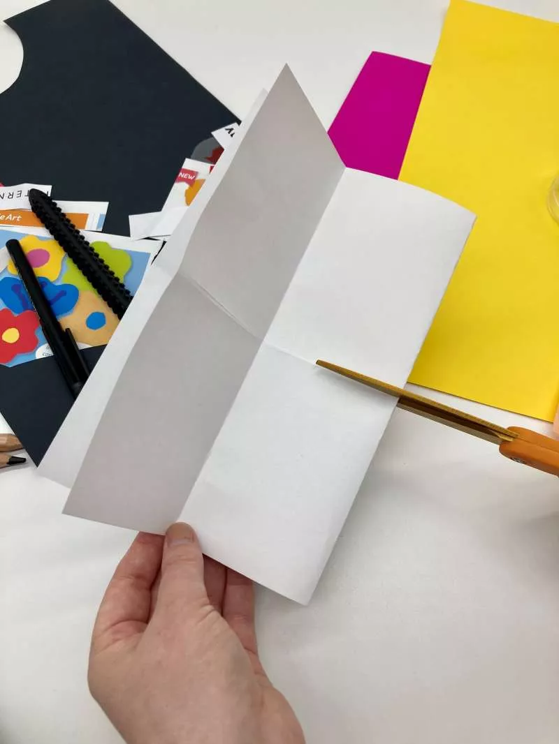A piece of A4 paper folder in half with someone cutting along a crease in the centre of the page. A piece of A4 paper folder in half with someone cutting along a crease in the centre of the page.