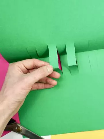 A green piece of paper opened up at the crease with two rectangles popping up from the middle. A green piece of paper opened up at the crease with two rectangles popping up from the middle.