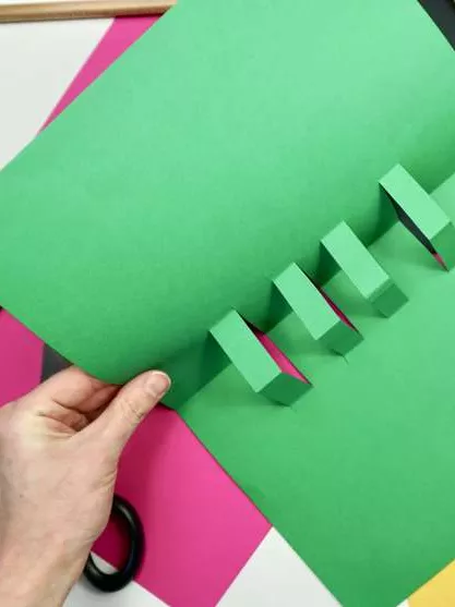 A green piece of paper with 4 rectangles popping out from the centre crease. A green piece of paper with 4 rectangles popping out from the centre crease.