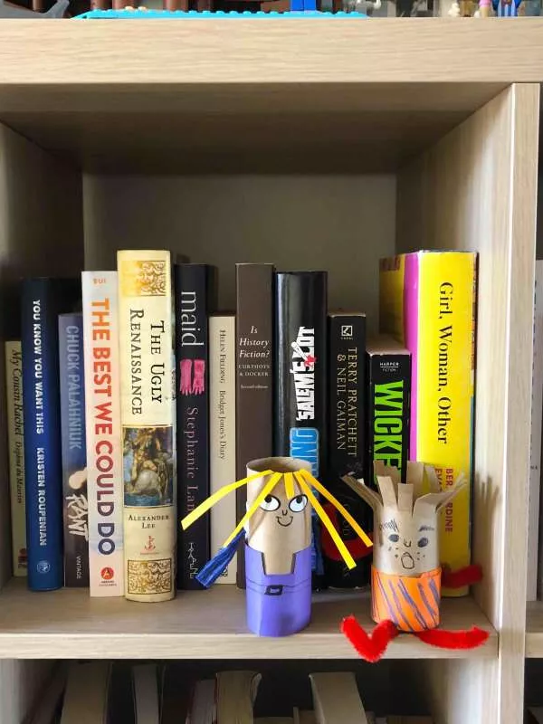 Two puppets made out of toilet rolls sit on a bookshelf. Two puppets made out of toilet rolls sit on a bookshelf.