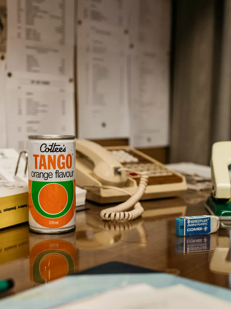 A can of 'Tango' drink sat on a desk, along with a telephone, hole punch and other typical clutter found on desks.