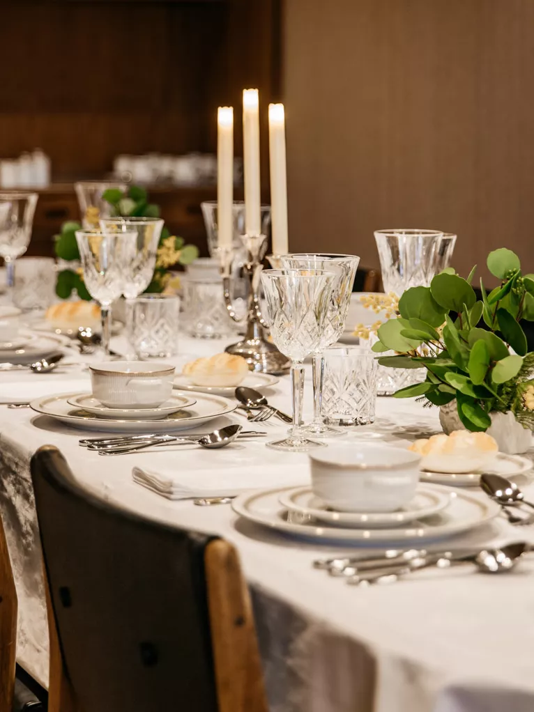 A dinner table set up with china, white linens, silverware and white candles ready for a dinner party