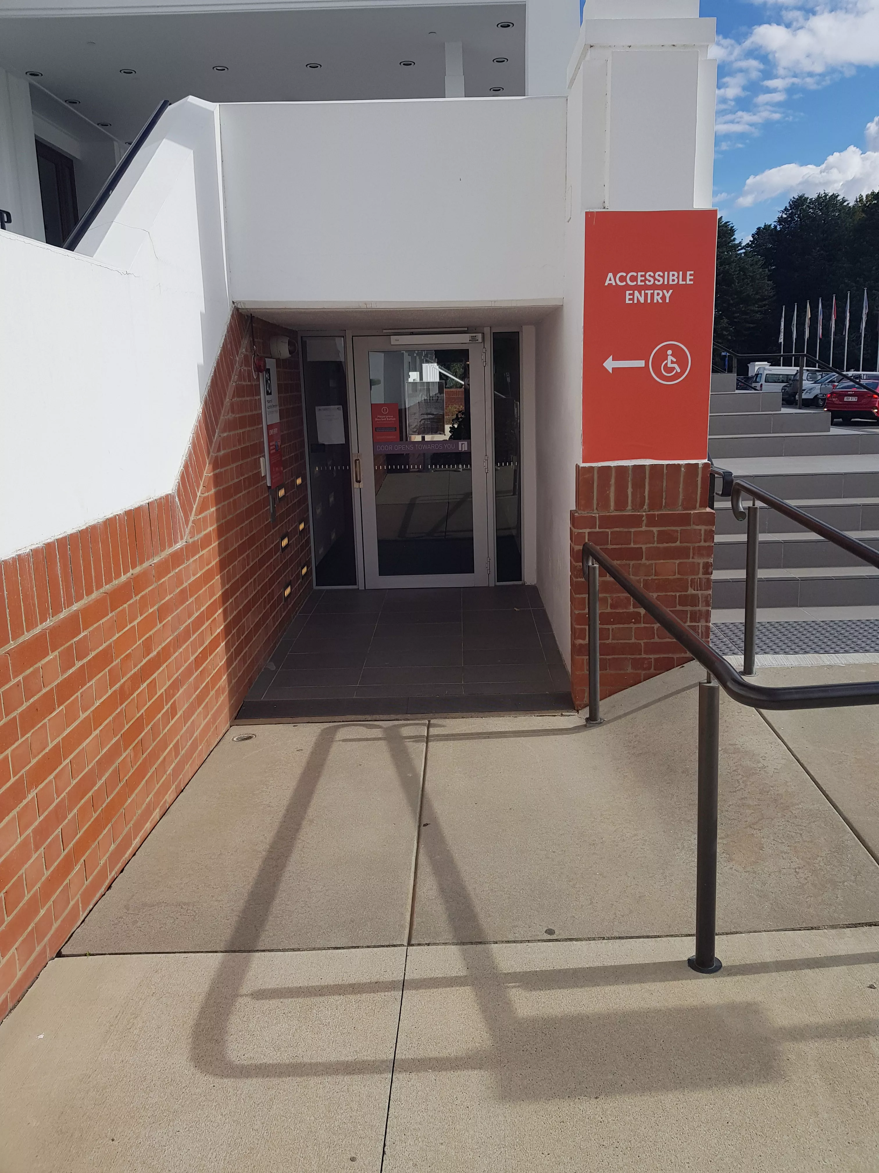 A flat path leading to a door at the side of a building with a red sign that reds 'accessible entry;. A flat path leading to a door at the side of a building with a red sign that reds 'accessible entry;.