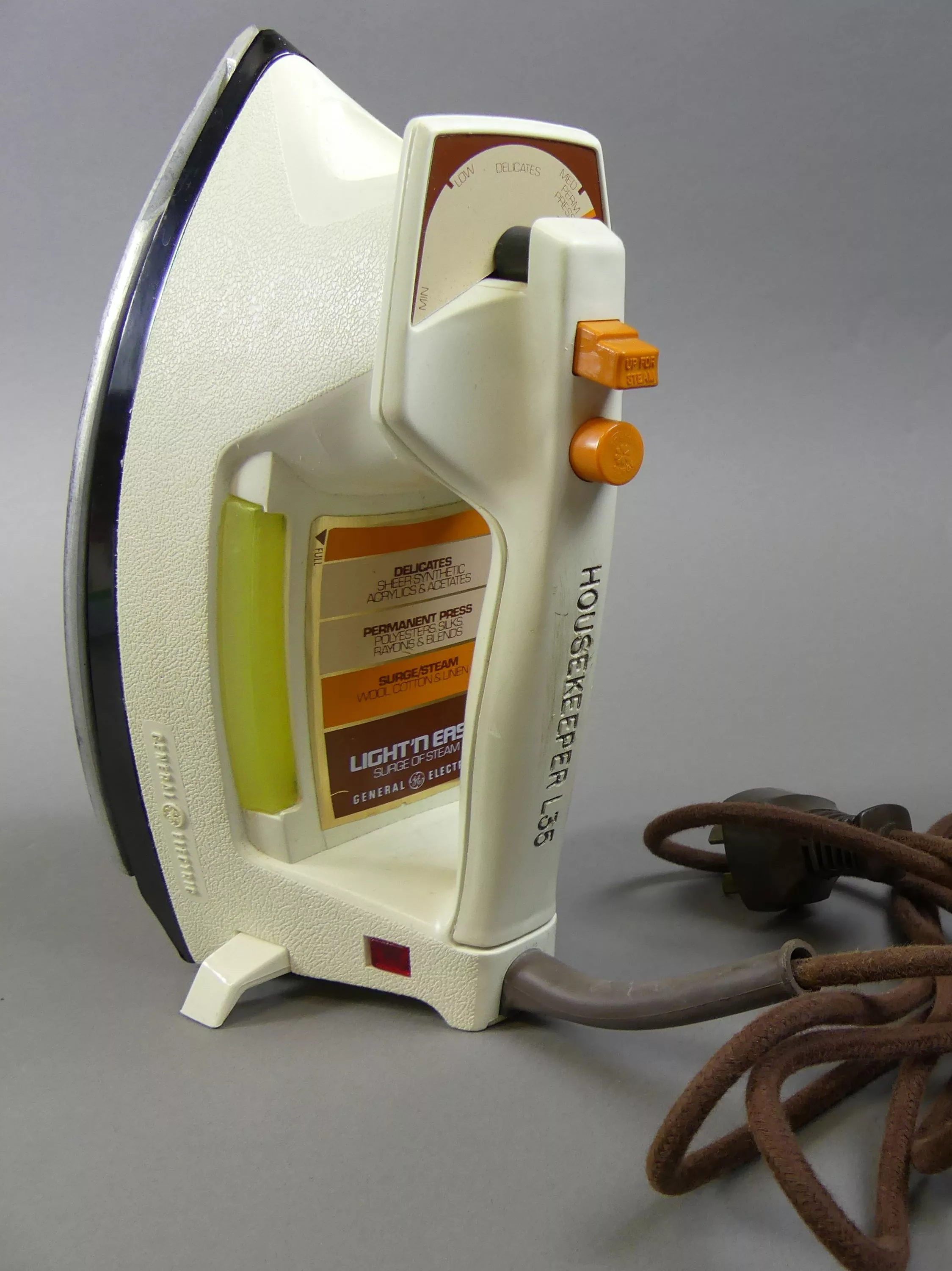 A white hand iron with orange buttons and a brown power cord.