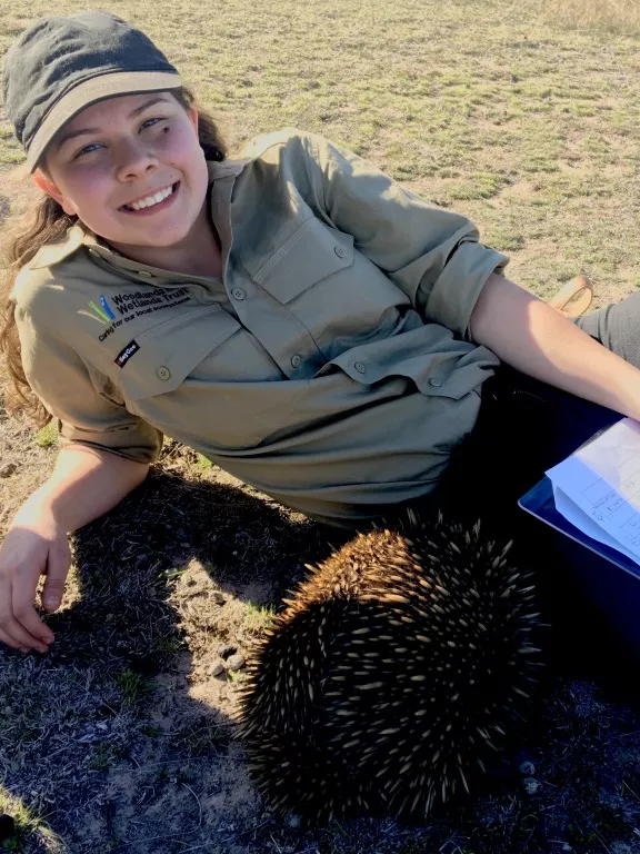 Dhani Gilbert lies on the ground, looking at the camera, with an echidna close to her Dhani Gilbert lies on the ground, looking at the camera, with an echidna close to her