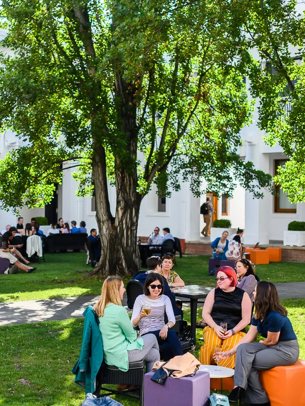 People sit on orange and purple cubes in the courtyard of Old Parliament House having drinks.