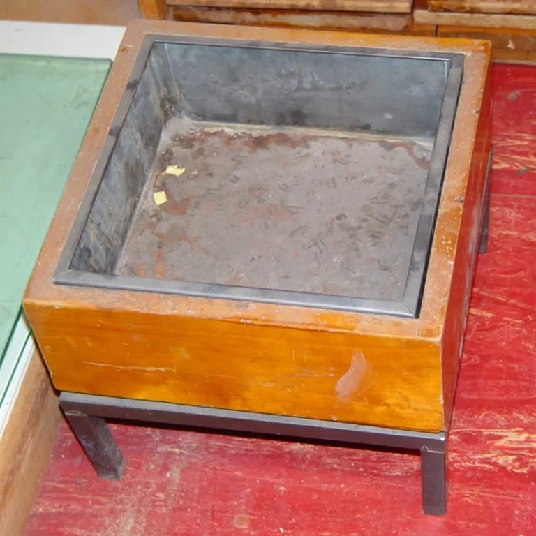 A square wooden ashtray with a metal insert and sitting on a metal base with four small legs.