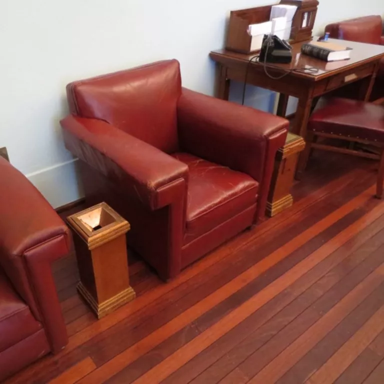 Rectangular wooden pedestal ashtray sitting between two red leather chairs.