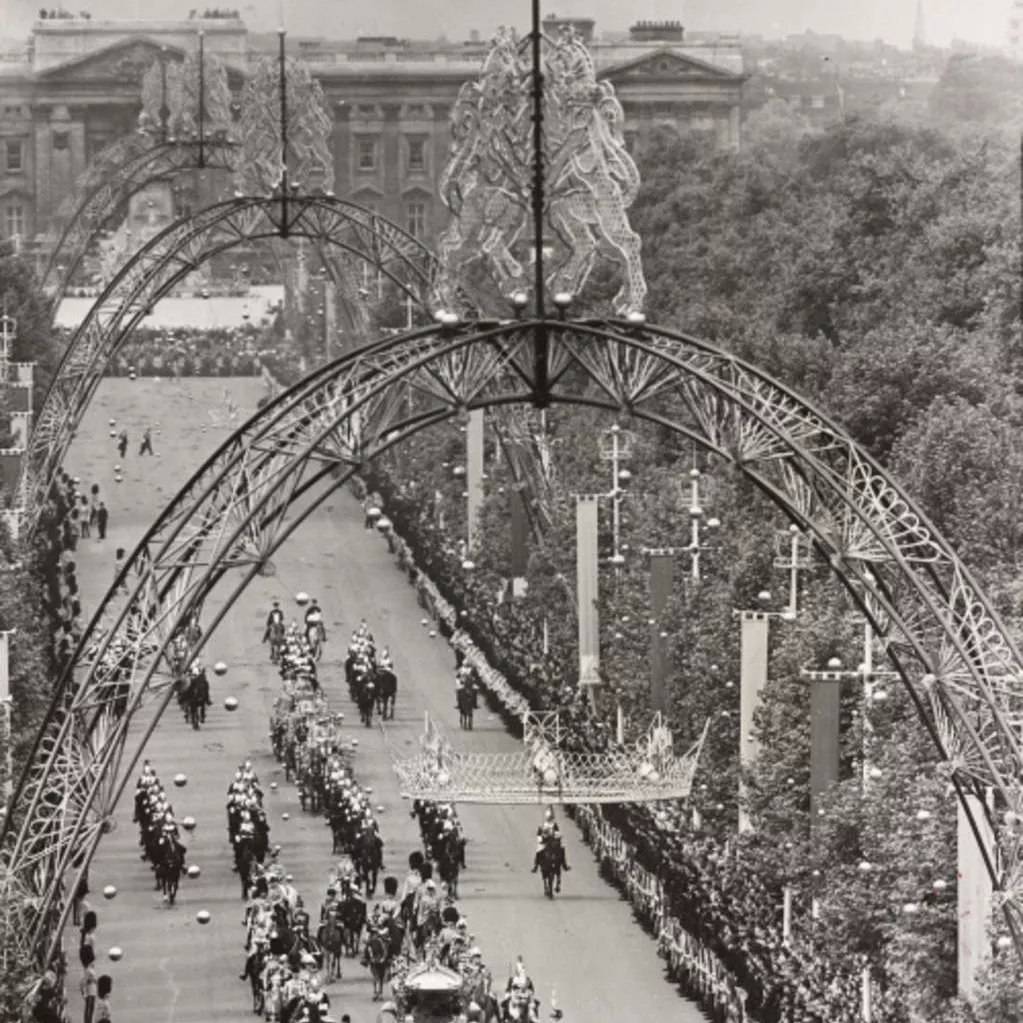 Queen Elizabeth II’s coronation procession proceeds down the Mall from Buckingham Palace underneath magnificent ornamental arches.