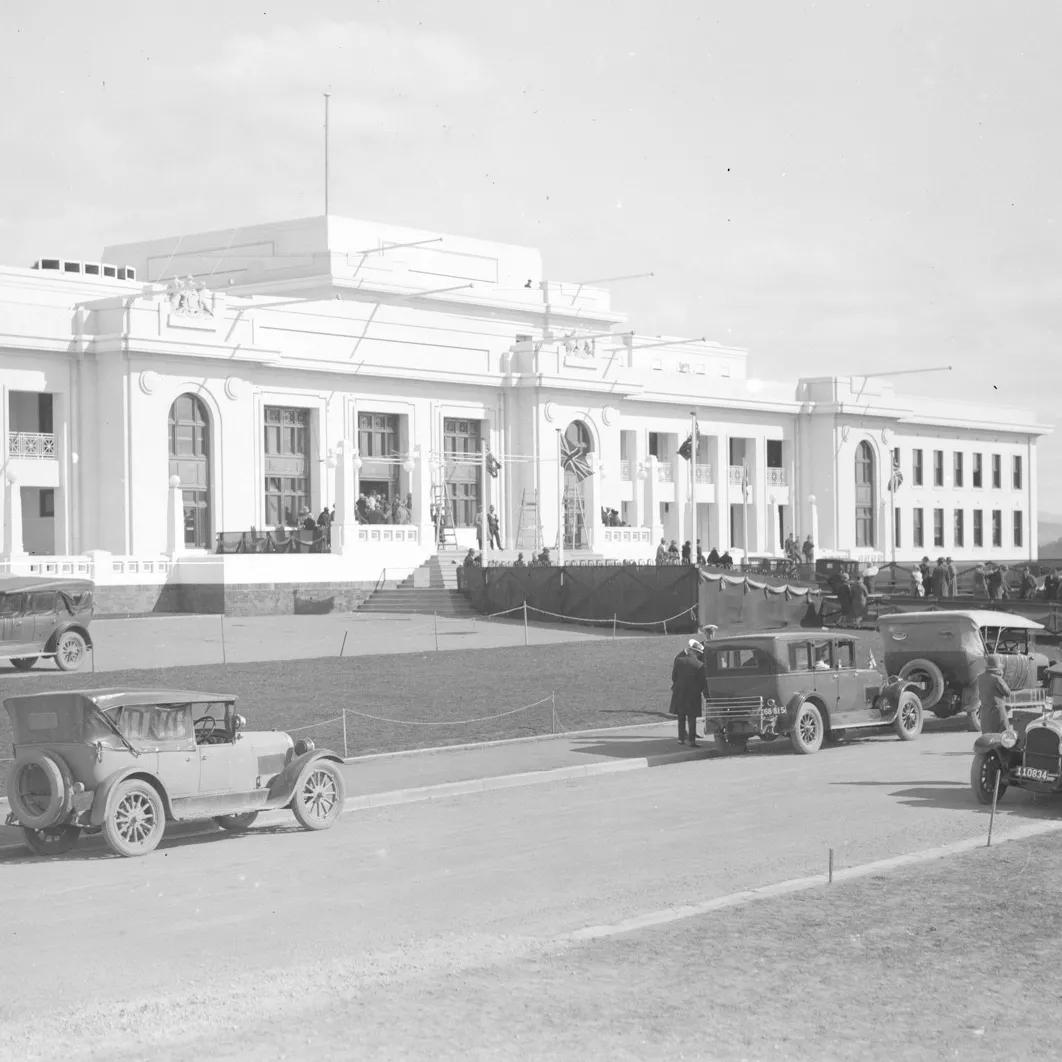 A black and white photo from 1927 of a large white building, Old Parliament House, with cars driving past.