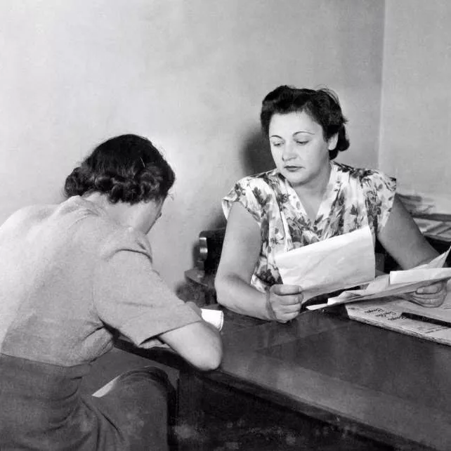 Nancy Wake, a short-haired woman, sitting at a desk, holding papers in her hand.