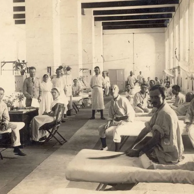 Earle Page (in the suit) standing a field hospital surrounded by medical staff and patients sitting in their beds.